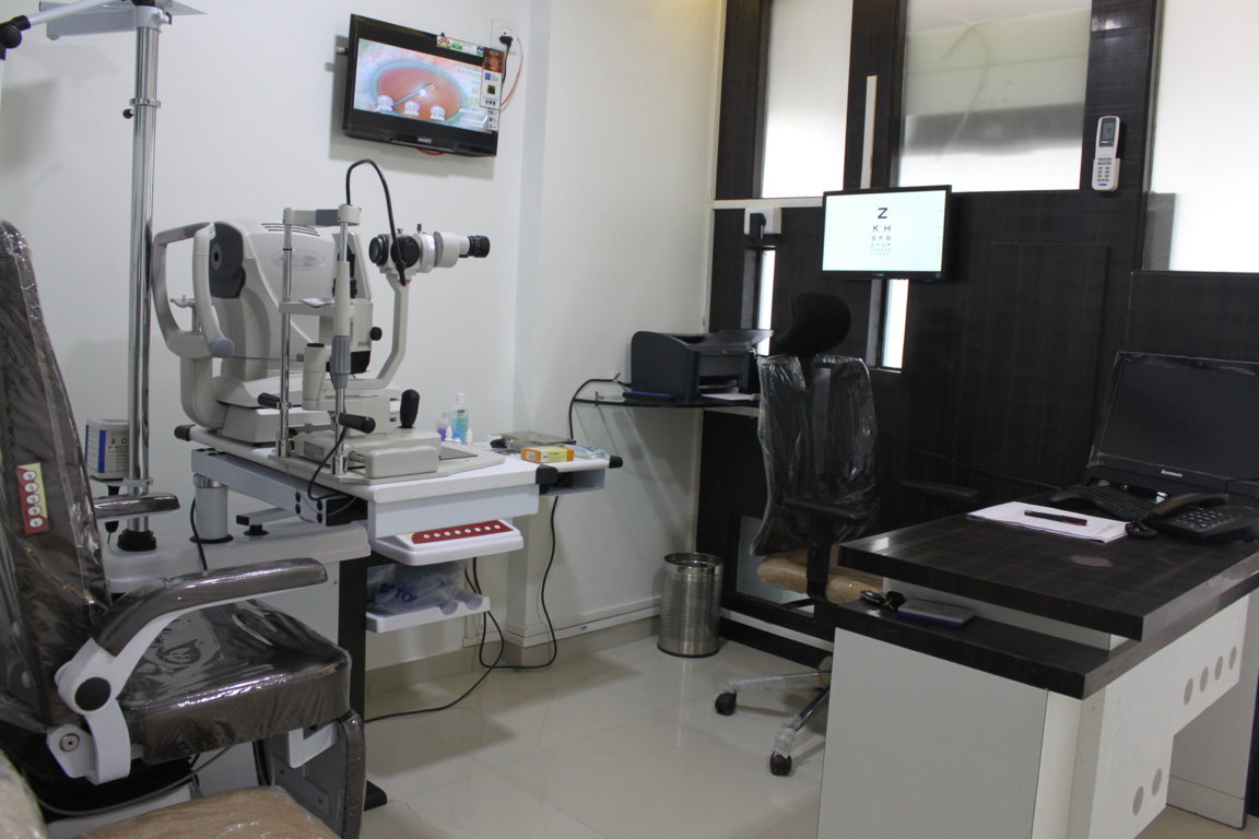 Doctor's slit-lamp examination chamber at Insight Institute with a Snellen acuity chart on the overhead monitor and a patient education screen on the side wall
